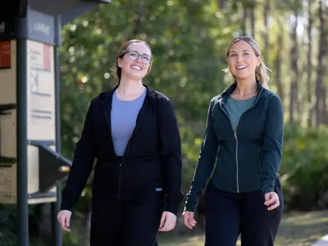 Two women walking together on a path, smiling and holding hands.