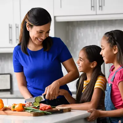 A mother and her two daughters are preparing vegetables together in the kitchen.