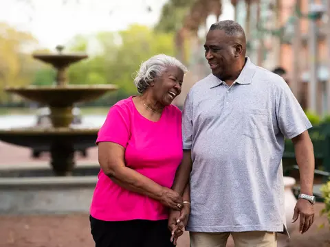 Elderly couple smiling and holding hands in front of a fountain.
