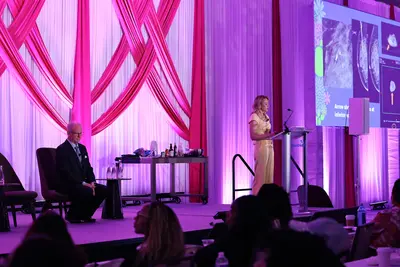 Speaker presenting medical imaging on stage to an audience during a women’s health conference.