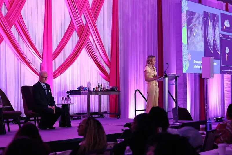 Speaker presenting medical imaging on stage to an audience during a women’s health conference.