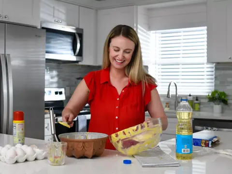 A woman in a red shirt is mixing ingredients in a bowl on a kitchen counter.