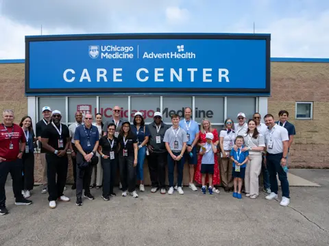 Large group of team members and guests pose in front of a UChicago Medicine and AdventHealth Care Center sign outside the building