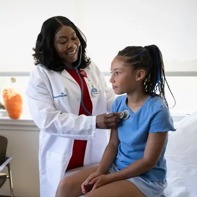A doctor is examining a young girl with a stethoscope while a woman watches.