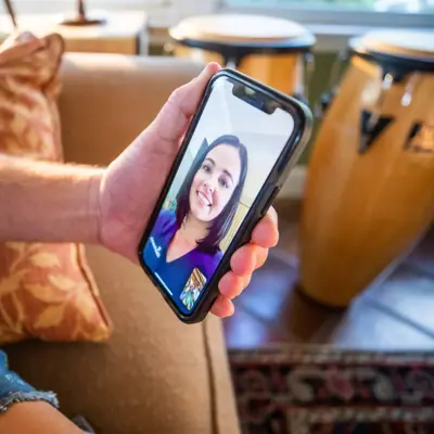 Person sitting on a couch holding a smartphone with a smiling woman on the screen.