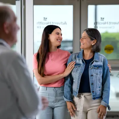 A doctor talks with two smiling women, one with her arm around the other.