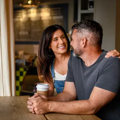 Smiling couple sharing an intimate moment at a coffee shop counter, woman holding a coffee cup while looking at her partner