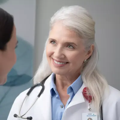 A smiling doctor with a stethoscope around her neck talks to a patient.