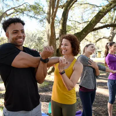 Group of people smiling and stretching outdoors, promoting a healthy lifestyle.