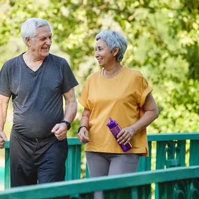An older couple in athletic wear walking together on a green bridge outdoors, smiling and enjoying each other's company during their exercise routine