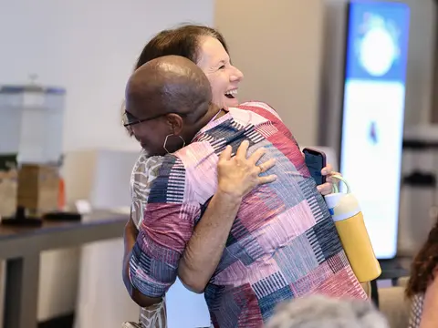 Two women sharing a hug and smiling at an event.