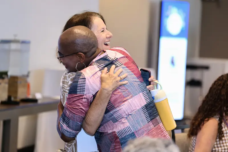 Two women sharing a hug and smiling at an event.