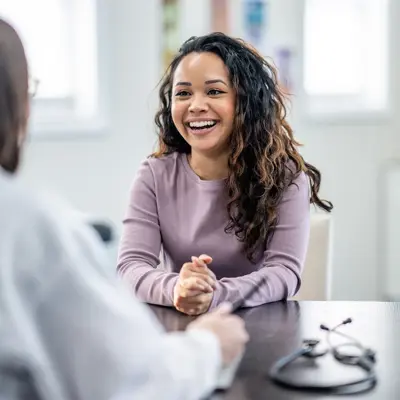Smiling woman in purple sweater sitting at a desk during a consultation with a healthcare provider in a bright medical office