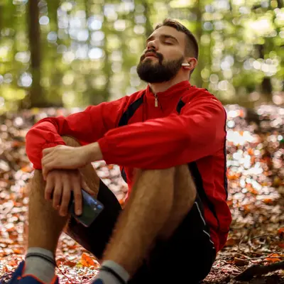 A man takes a break from a run, sitting on the ground outdoors.