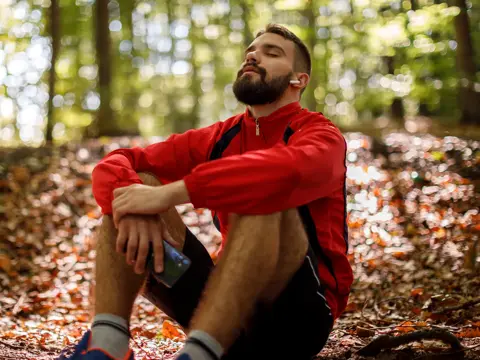 A man takes a break from a run, sitting on the ground outdoors.