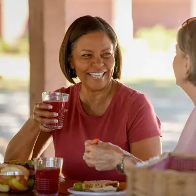 Two women sitting at a picnic table, smiling and enjoying a meal together.