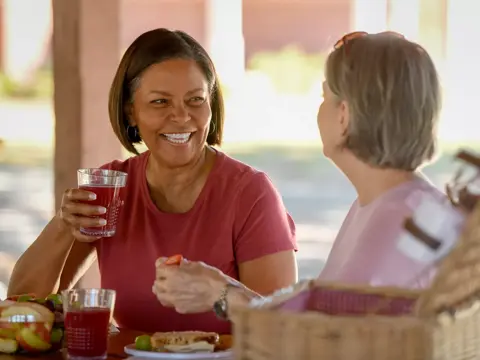 Two women sitting at a picnic table, smiling and enjoying a meal together.