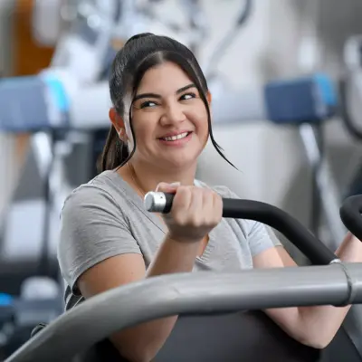 Smiling woman in gray shirt using a weight machine in a gym.