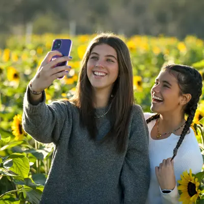 Two smiling women taking a selfie in a sunflower field, showcasing joy and connection.
