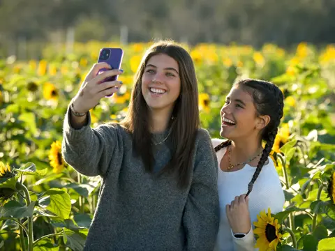 Two smiling women taking a selfie in a sunflower field, showcasing joy and connection.