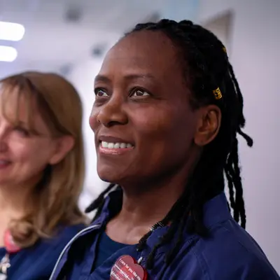 Three smiling healthcare workers in blue uniforms stand together in a hospital corridor.