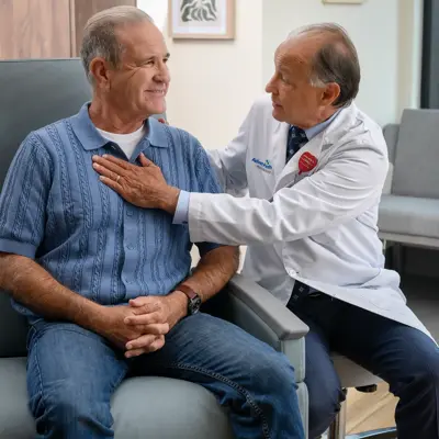 A doctor in a white coat examines a smiling patient seated on a chair, conveying a sense of care and comfort.