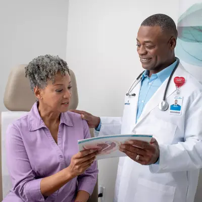 Doctor in white coat and stethoscope explaining a medical diagram to a seated patient.