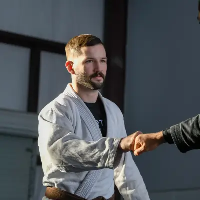 Two men in martial arts uniforms shake hands in a gym setting, showcasing sportsmanship.