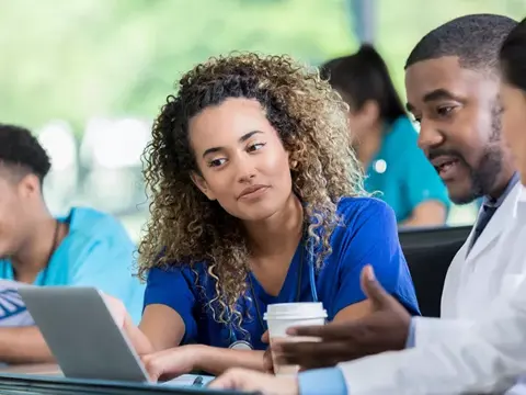 Group of healthcare professionals collaborating around a laptop, discussing patient care.
