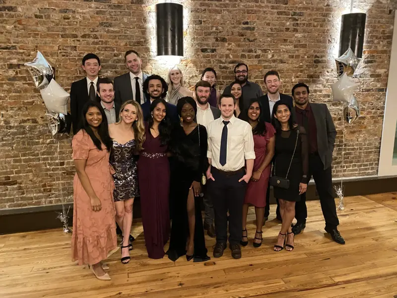 Group dressed in formal attire posing indoors against a brick wall with star-shaped balloons.