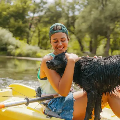 A Young woman kayaking down the river and enjoying beautiful nature that surrounds it with a dog.