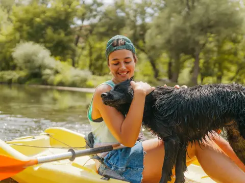 A Young woman kayaking down the river and enjoying beautiful nature that surrounds it with a dog.
