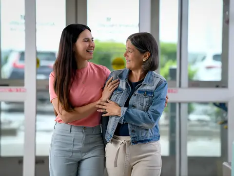 Two smiling women embracing each other in a hospital corridor, showcasing warmth and support.