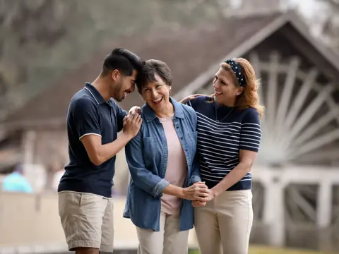 Three smiling individuals, two women and a man, standing together in front of a building.